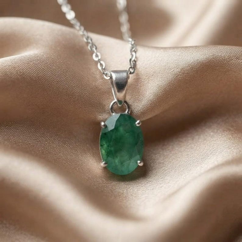 Beautiful Dainty Emerald Necklace featuring a 10–15Ct natural green gemstone in an elegant oval-cut design. The faceted emerald pendant catches the light while its natural inclusions and variations give the gemstone a unique appearance. This May birthstone necklace can be worn with everyday clothing, business outfits, evening dresses, wedding attire, and layered jewelry styles, making it an elegant gift for birthdays, anniversaries, Mother's Day, and special celebrations.
