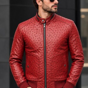 Puede incluir: Una chaqueta de color rojo vibrante con un patrón texturizado de piel de avestruz, cuello alzado con cierre de botón a presión, cremallera frontal negra completa y puños y dobladillo acanalados. La chaqueta incluye dos bolsillos delanteros con botones.