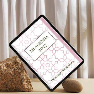 Puede incluir: Una tableta digital que muestra la portada de una agenda con un patrón geométrico rosa y el texto MI AGENDA 2027 y Descarga instantánea. La pantalla presenta un fondo blanco con un diseño de líneas rosas repetitivo y una etiqueta central.