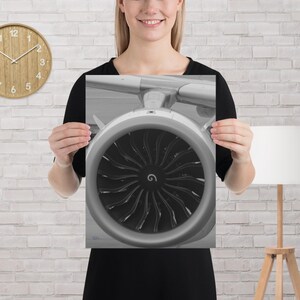 Puede incluir: Una impresión en blanco y negro que muestra un primer plano de la entrada de un gran motor a reacción. La carcasa circular rodea un ventilador oscuro con numerosas palas curvas que irradian desde un eje central, mostrando el diseño mecánico.