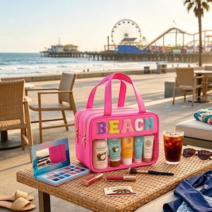 May include: A bright pink rectangular cosmetic bag with the word BEACH in colorful, textured letters on the front. The bag features a clear window displaying five skincare tubes, a makeup palette, two lip glosses, a brush, and sunglasses.