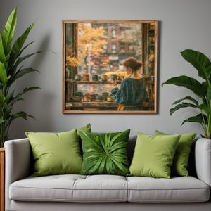 May include: A square framed wall art piece depicting a person in a blue shirt standing before a window filled with various ceramic mugs, overlooking a city street with autumn trees. The artwork is displayed above a light gray sofa with green pillows.