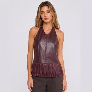 May include: A sleeveless halter top in a deep burgundy colour, crafted from a smooth material with a visible vertical seam down the centre. The garment features a straight hemline adorned with a long, matching fringe that hangs to the waist.