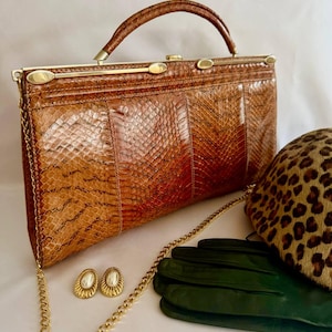 May include: A brown snakeskin-patterned handbag with a gold-tone metal frame, a top handle, and a detachable gold chain strap. Beside it are a pair of oval gold-tone earrings with white centers, dark green leather gloves, and a leopard-print hat.