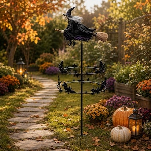 May include: A black metal garden stake featuring a sculpted witch figure in a pointed hat riding a broomstick at the top, positioned above two circular tiers decorated with metal bat and star silhouettes, supported by a thin vertical pole.