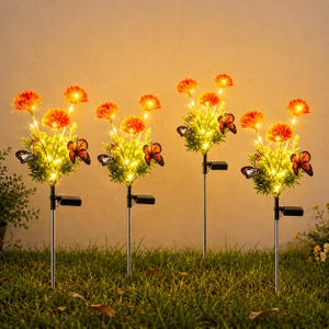 Puede incluir: Cuatro luces solares de jardín con estacas, flores de caléndula artificiales de color naranja y mariposas decorativas. Cada estaca tiene un pequeño panel solar en el tallo y luces LED de color blanco cálido que iluminan las flores.