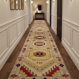 Pode incluir: Um tapete passadeira retangular longo com uma base de cor creme e um padrão geométrico repetitivo em tons de vermelho, amarelo, azul claro e castanho escuro. O tapete tem extremidades com franjas e um design simétrico com motivos octogonais.