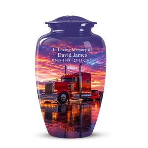 May include: A purple cremation urn featuring a sunset scene with a red semi-truck. The text reads: In Loving Memory of David James 02-08-1998 - 25-11-2025. The urn has a smooth, glossy finish and a matching lid, displaying a reflective surface.