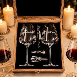 Puede incluir: Una caja de regalo de madera que contiene dos copas de vino transparentes grabadas con los nombres Miriam y Emmanuel, un sacacorchos plateado, un tapón de botella de metal y un vertedor, sobre un forro de terciopelo negro.