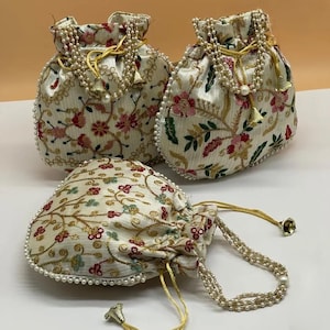 May include: Three off-white drawstring pouches featuring intricate floral embroidery in shades of pink, red, and green. Each bag is accented with gold metallic thread, small white faux pearl bead trim, and long gold cord handles with bell-shaped ends.
