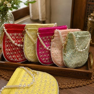 May include: A collection of six drawstring pouches in red, yellow, magenta, peach, and light green satin fabric. Each pouch features a diamond-quilted pattern with small white floral beadwork, a white pearl bead handle, and gold-toned cord accents.