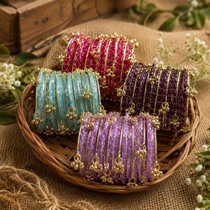 Può includere: Quattro set di braccialetti impilati in rosa brillante, azzurro, viola scuro e lavanda. Ogni braccialetto presenta una superficie testurizzata e sfaccettata, decorata con piccoli ciondoli in metallo dorato pendenti a intervalli regolari.