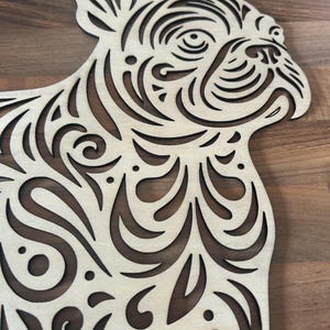 May include: A light-colored wooden cutout of a French Bulldog silhouette featuring intricate, laser-cut scrollwork and swirling patterns throughout the body, head, and ears, creating a detailed openwork design across the entire surface.