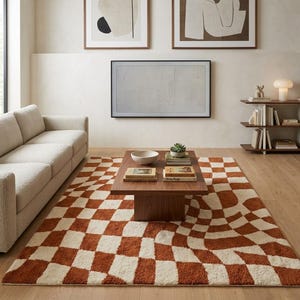 May include: A rectangular area rug featuring a distorted, wavy checkerboard pattern in burnt orange and cream. The rug is positioned on a light wood floor beneath a low-profile wooden coffee table, extending across the living room floor space.