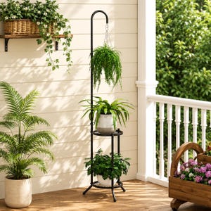 May include: A tall, black metal plant stand featuring a curved top hook for a hanging basket, two circular shelves for potted plants, and a tripod base. The stand holds a hanging fern, a potted green plant, and a small leafy plant.