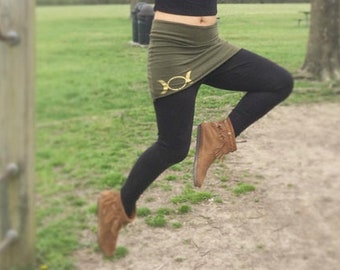 May include: A person wearing a black top, olive green skirt, and black leggings hangs from a monkey bar set. The skirt has a gold design. The person is also wearing brown boots and sunglasses.