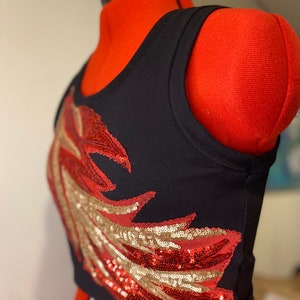 May include: A black tank top with a red and gold sequined wing design. The tank top is cropped and has a sleeveless design.