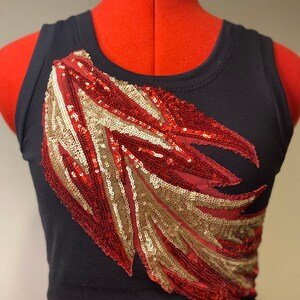 May include: A black tank top with a red and gold sequined design on the front. The design is a stylized feather shape.