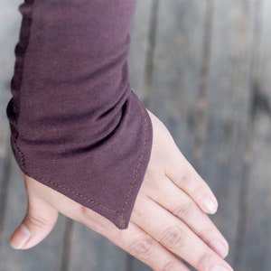 May include: A close-up of a dark brown sleeve with a distinctive pointed cuff design. The cuff is stitched with a contrasting thread. The fabric appears soft and slightly gathered.