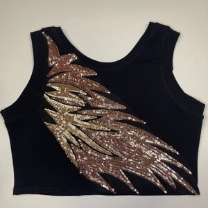 May include: A black tank top with a large gold and rose gold sequined design on the front. The design is a stylized feather shape.