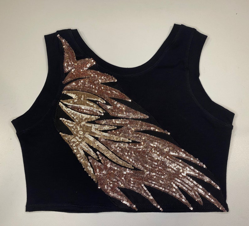 May include: A black tank top with a large gold and rose gold sequined design on the front. The design is a stylized feather shape.