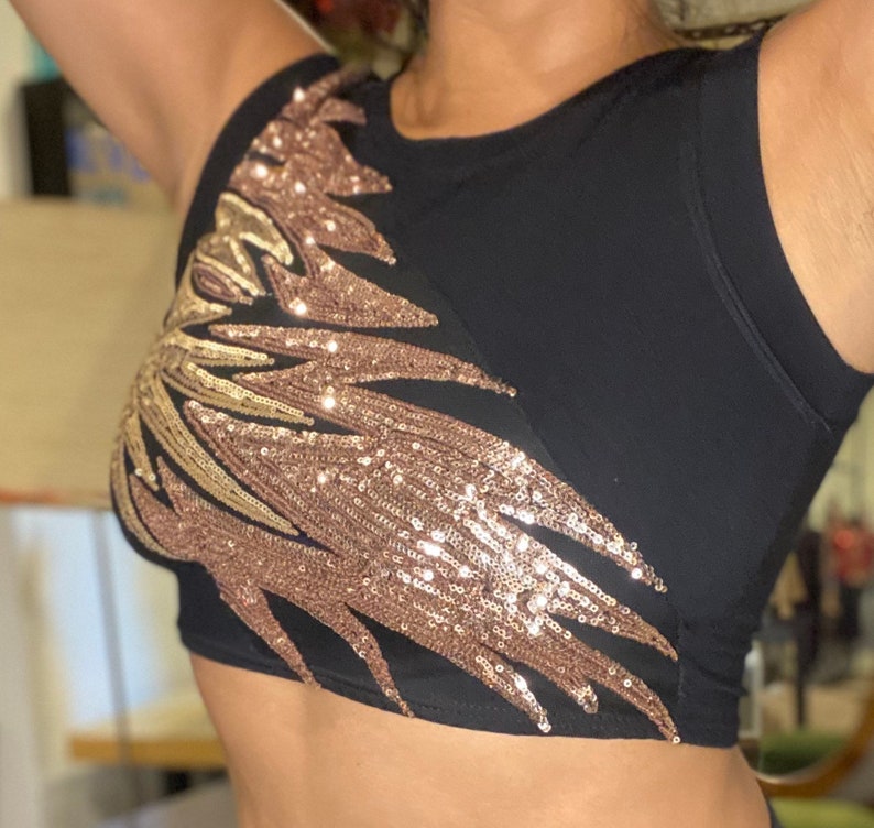 May include: A black crop top with a gold and rose gold sequin design on the front. The design is a large, abstract shape that covers most of the front of the top.