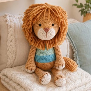 Può includere: Un leone di peluche all'uncinetto con corpo color marrone chiaro, una folta criniera in filato marrone dorato e un busto a righe nei toni dell'azzurro e del turchese. Il leone ha piccoli occhi a perla neri, naso ricamato rosa e zampe bianche.