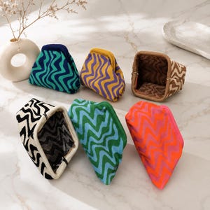 May include: Six small, soft-sided pouches with a flexible frame opening, each featuring a distinct two-tone wavy pattern. The color combinations include teal and navy, yellow and purple, brown and beige, black and white, green and blue, and orange and pink.