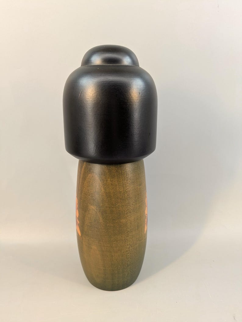 May include: A wooden pepper mill featuring a smooth, matte black top section and a cylindrical base with a natural olive-green wood grain finish. The base displays a subtle, light-colored floral pattern etched into the wood surface.