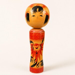 K&ouml;nnte beinhalten: Eine h&ouml;lzerne Kokeshi-Puppe mit einem kugelf&ouml;rmigen Kopf, bemaltem Gesicht, schwarzem Haar und orangefarbenen Blumenakzenten. Der zylindrische K&ouml;rper ist in Gelb- und Rott&ouml;nen mit schwarzen und orangefarbenen Blumenmustern und glatter Oberfl&auml;che.