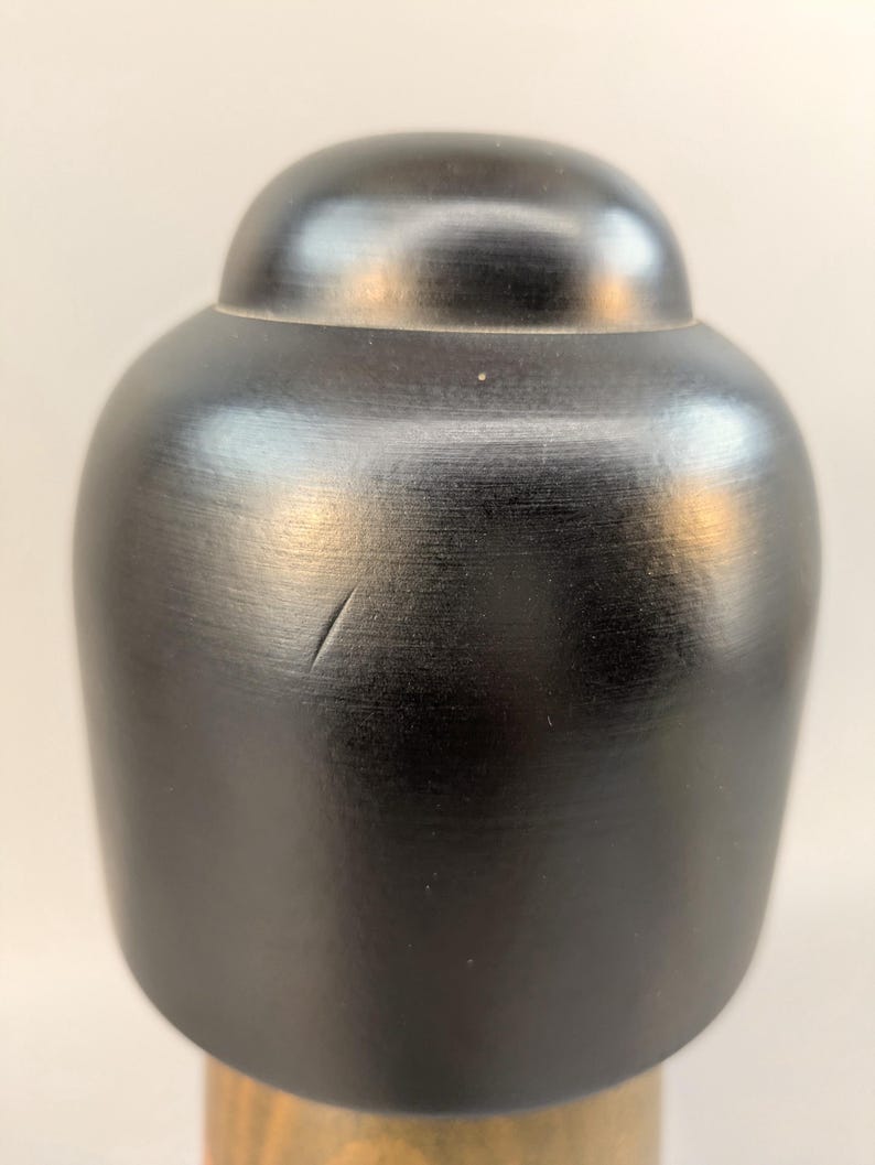 May include: A smooth, matte black, rounded wooden cap with a small, thin scratch on its surface. The cap features a domed top section that transitions into a wider, cylindrical base, showcasing a dark, uniform finish with subtle wood grain.