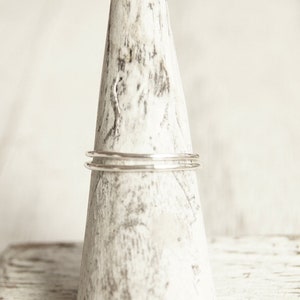 May include: Three thin silver rings stacked on a white wooden ring holder.