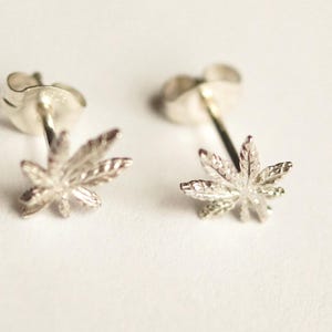 May include: A pair of silver stud earrings featuring a detailed marijuana leaf design.
