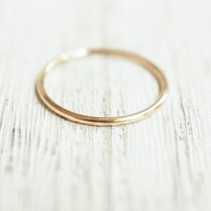 Peut inclure: Une simple bague en or, posée sur une surface en bois blanc.