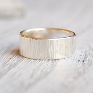May include: A silver ring with a textured, hammered finish. The ring is wide and has a rounded shape.