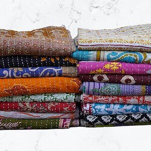 May include: A stack of folded rectangular fabric quilts featuring various patterns and colors including mustard yellow, deep blue, vibrant pink, orange, green, and black. Each quilt displays intricate white running stitch embroidery details.