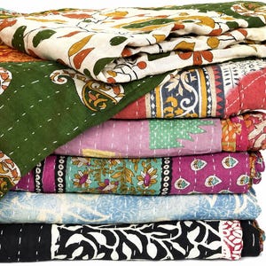 May include: A stack of folded cotton quilts featuring various block-printed patterns in colors including green, orange, pink, blue, and black. Each quilt displays intricate kantha stitching throughout, creating a textured surface on the fabric.