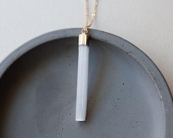 May include: A gold chain necklace with a white selenite crystal pendant. The pendant is a long, thin rectangle with a gold top.
