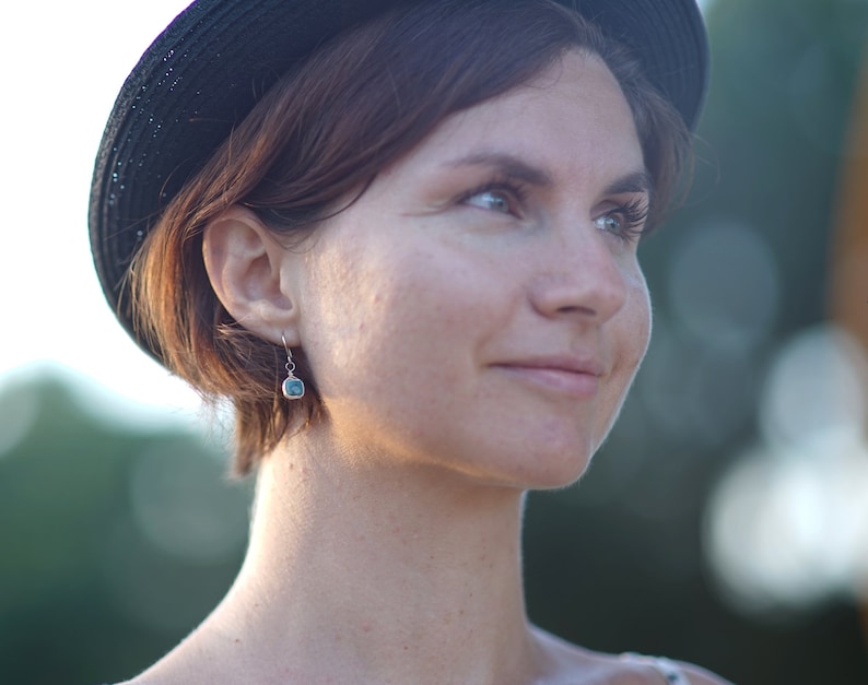 May include: A woman with short brown hair wearing a black hat and a silver earring with a blue stone.