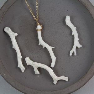 Puede incluir: Un collar de cadena dorada con un colgante de coral blanco. El colgante est&aacute; hecho de varias ramas de coral, y la cadena es delicada y simple.