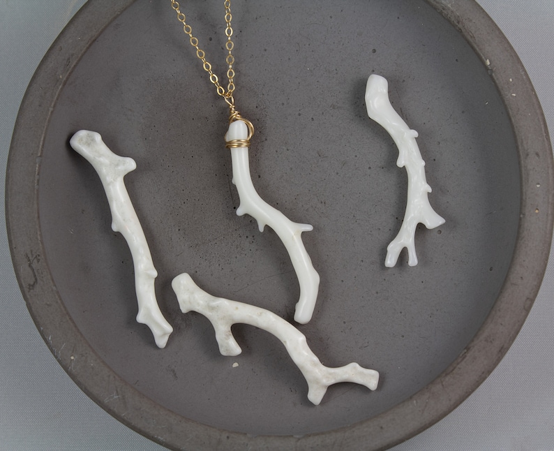 Puede incluir: Un collar de cadena dorada con un colgante de coral blanco. El colgante est&aacute; hecho de varias ramas de coral, y la cadena es delicada y simple.