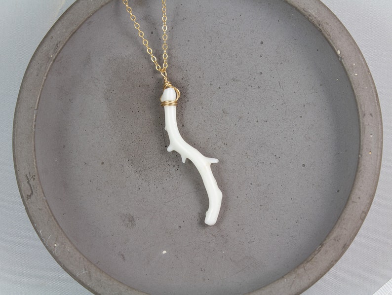 Puede incluir: Un delicado collar con un colgante de rama de coral blanco y una cadena de oro. La rama de coral tiene una forma natural y una textura &uacute;nica.