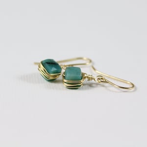 May include: A pair of gold wire wrapped earrings with teal green gemstone accents.