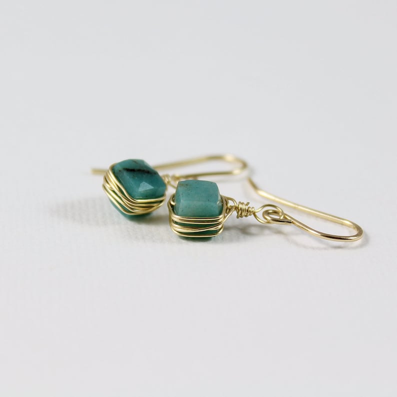 May include: A pair of gold wire wrapped earrings with teal green gemstone accents.