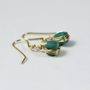 May include: A pair of gold wire wrapped earrings with teal green gemstone accents.
