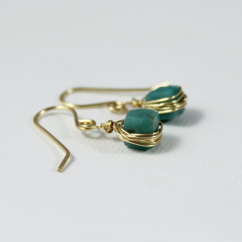May include: A pair of gold wire wrapped earrings with teal green gemstone accents.