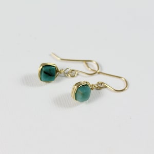 May include: A pair of gold wire wrapped earrings with teal green gemstone accents.