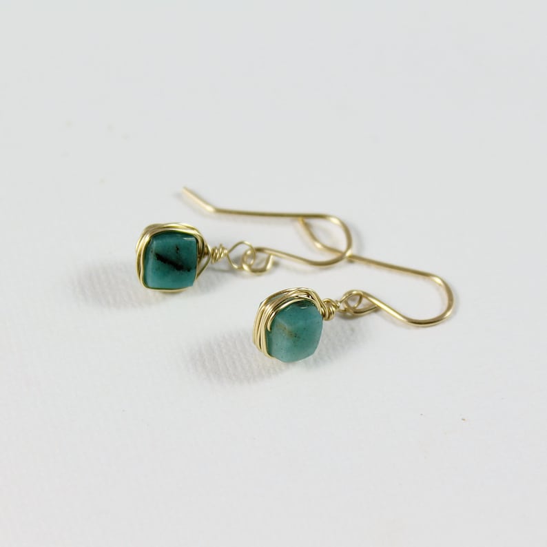 May include: A pair of gold wire wrapped earrings with teal green gemstone accents.