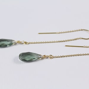 Może przedstawiać: Para złotych kolczyków z łańcuszkiem i zielonymi kamieniami szlachetnymi w kształcie łzy.