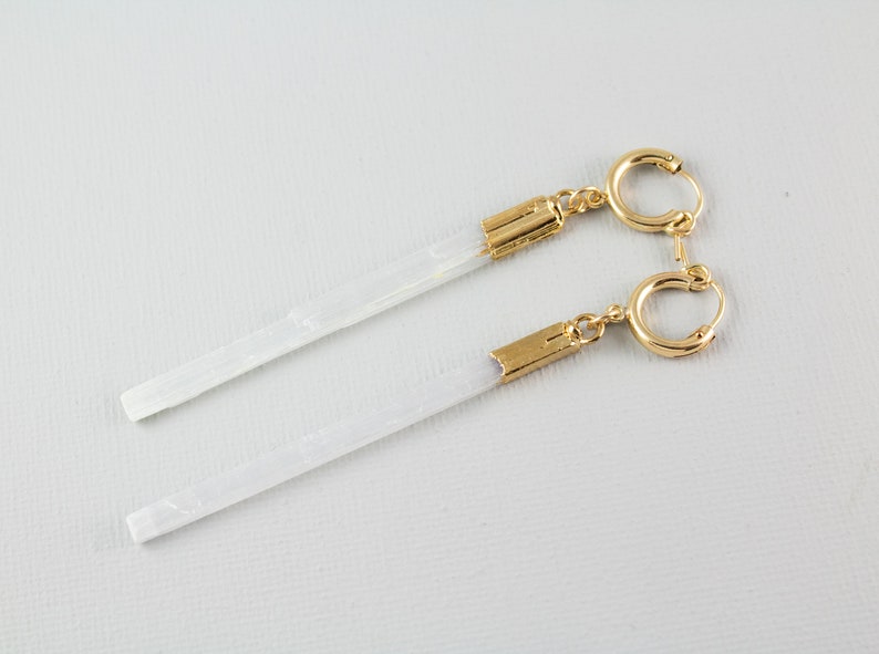 Puede incluir: Un par de pendientes de aro dorados con colgantes de cristal blanco en forma de l&aacute;grima. Los pendientes est&aacute;n sobre un fondo blanco.